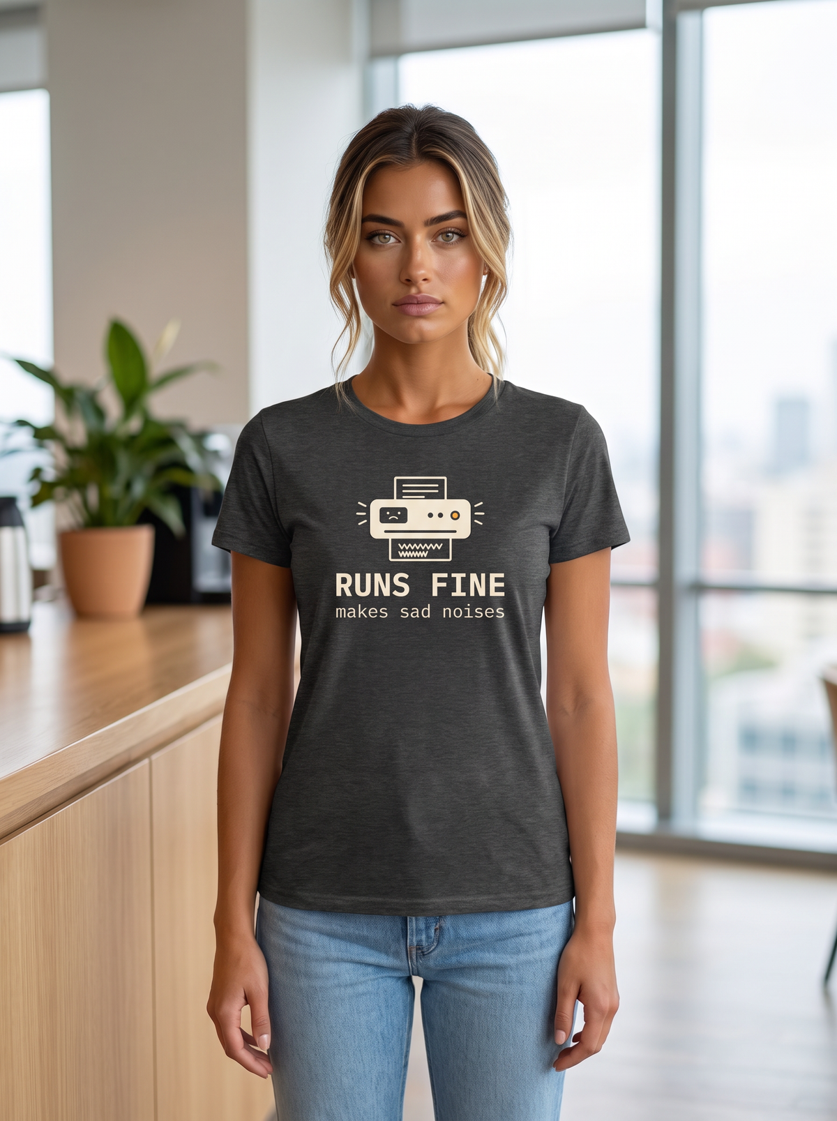 Seloura wearing the unisex t-shirt in dark grey heather with a drawing of an office printer with a sad face display and monospace type reading runs fine, makes sad noises. Model: Seloura (AI brand character). AI-generated model image; the printed design is the actual product artwork.