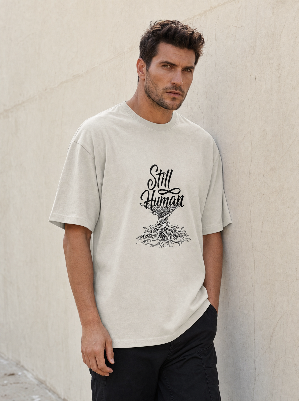 Still Human oversized faded tee in bone, worn against a plaster wall by Liora, Printelier's male brand character. AI-generated model image; the printed design is the actual product artwork.